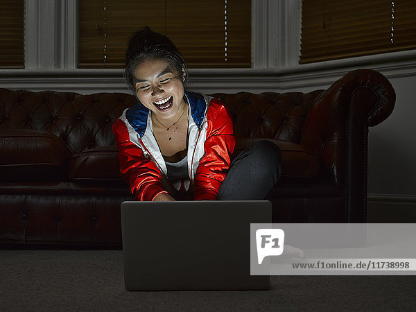 Junge Frau sitzt auf dem Boden und lacht über digitales Tablet