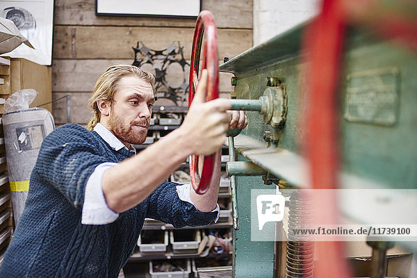 Junger Mann dreht Druckmaschinenräder in traditioneller Druckwerkstatt