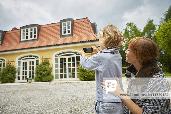 Junge mit einer mittel-erwachsenen Frau  die ein Smartphone benutzt  um ein Haus zu fotografieren