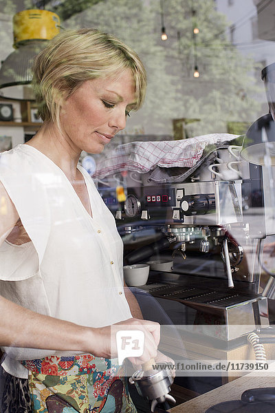 Mid adult woman making coffee in cafe
