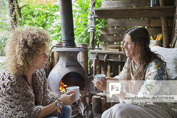 Two female friends drinking coffee in open cabin with wood stove