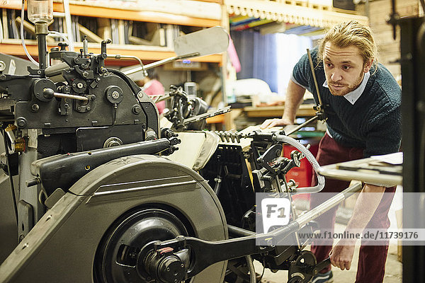 Junger Mann bedient alte Druckmaschine in traditioneller Druckwerkstatt