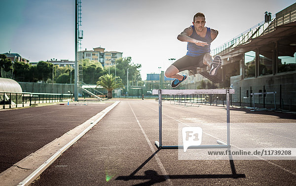 Mid adult man jumping over hurdle
