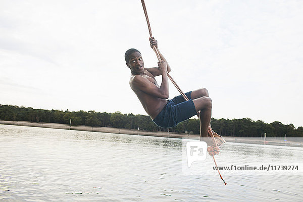 Young man rope swinging above lake