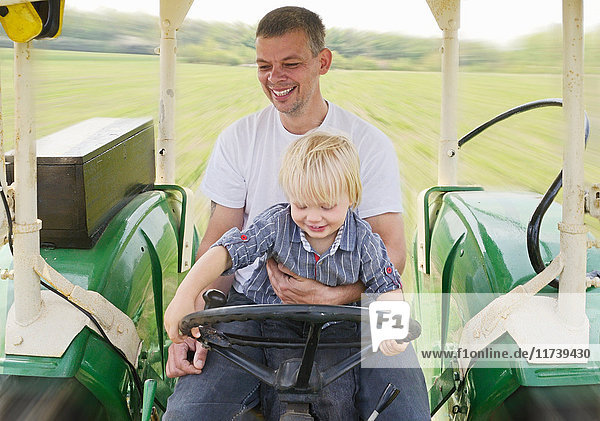 Reifer Mann sitzt mit seinem Sohn im Traktor und lächelt