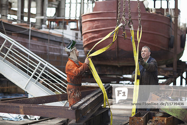 Workers using winch for girders in shipyard workshop
