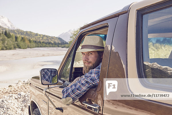 Mittelgroßer erwachsener Mann sitzt im Lastwagen  lehnt sich aus dem Fenster und schaut in die Kamera