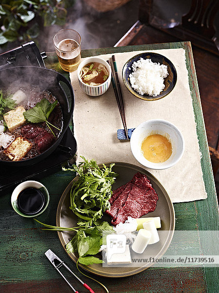 Still life of plate with salad leaf and meat with bowl of rice and sukiyaki