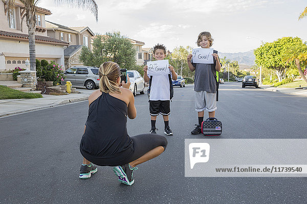 Mother photographing two schoolboy sons holding papers with handwritten school grade
