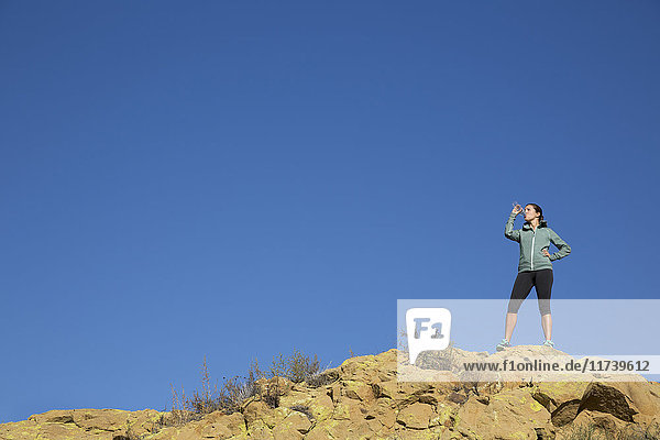 Female runner drinking from water bottle on rugged hill