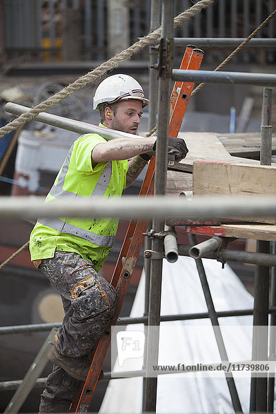Worker climbing scaffold ladder in shipyard
