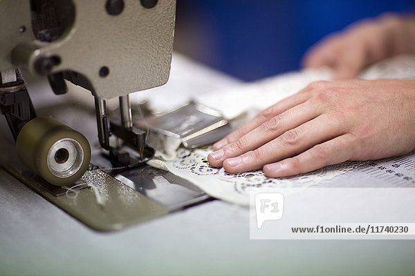 Hände eines männlichen Textildesigners bei der Benutzung einer Nähmaschine in einer alten Textilfabrik