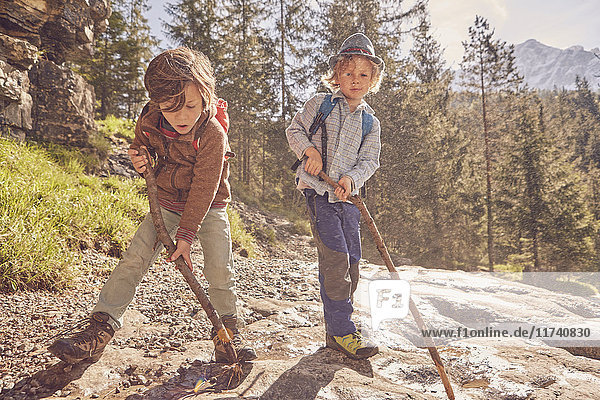 Two young boys  holding sticks  exploring forest