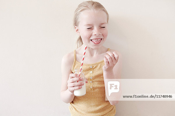 Young girl sticking tongue out and holding glass of milk