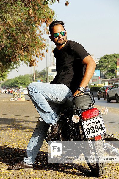 Young  stylish Indian man wearing goggles standing with his motorbike.