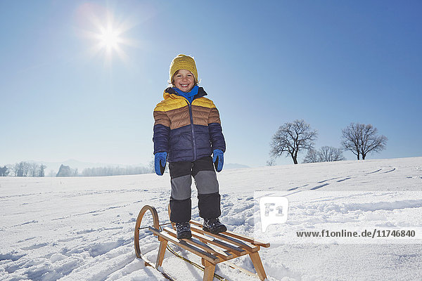 Porträt eines auf einem Schlitten stehenden Jungen in verschneiter Landschaft