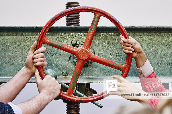 Männer- und Frauenhände drehen das Rad der Druckpresse in einer traditionellen Druckwerkstatt