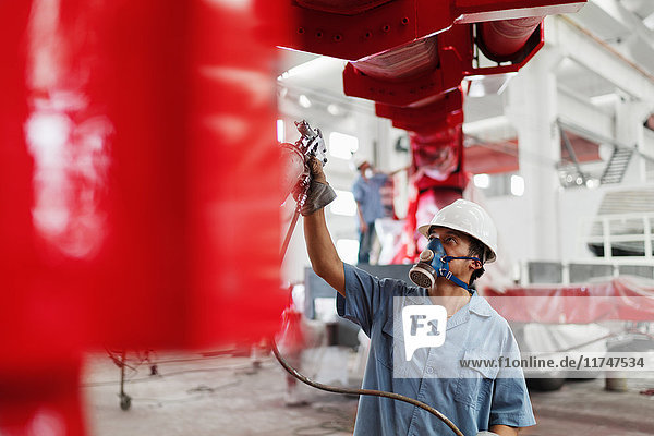 Male factory worker spray painting a red crane in factory workshop  China