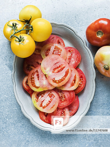 Stilleben von in Scheiben geschnittenen roten Tomaten in der Schale und gelben Strauchtomaten