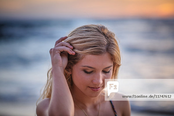 Young woman with hand in hair on beach at sunset