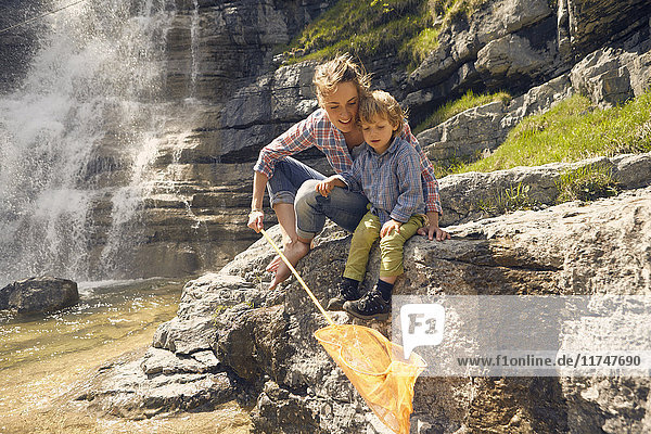Mutter und Sohn  auf Felsen am Wasserfall sitzend  mit Netz fischen