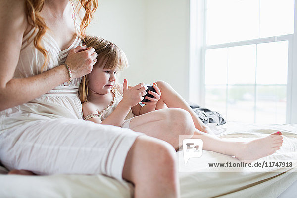 Woman and girl sitting on bed looking at smartphone