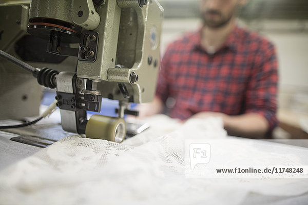 Männlicher Weber näht Spitze auf Nähmaschine in alter Textilfabrik