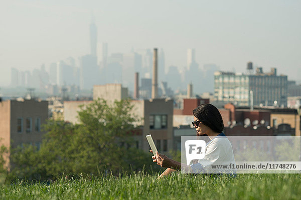 Mittelgroße erwachsene Frauen mit digitalem Tablet im Sunset Park mit der Skyline von Manhattan