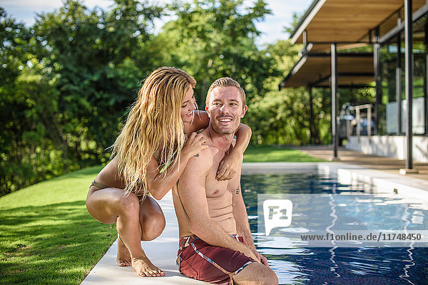 Young woman with arms around boyfriend at holiday apartment swimming pool