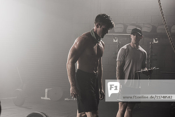 Bare chested  mid adult man  standing with trainer in gym