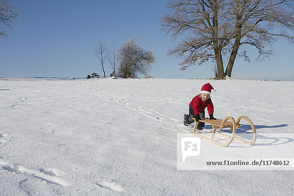 Young boy pushing sled down hill