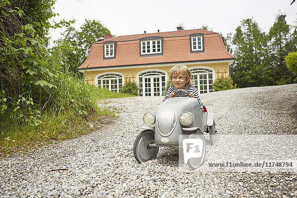 Junge spielt mit Oldtimer-Spielzeugauto auf der Auffahrt vor dem Haus