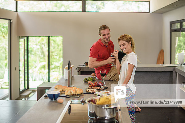 Couple preparing food and drinking red wine in kitchen
