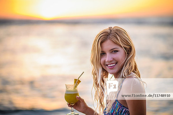 Portrait of young woman drinking cocktail on beach at sunset