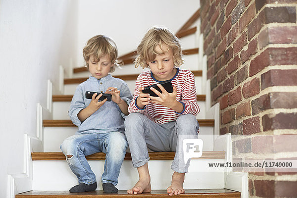 Zwei junge Brüder sitzen auf einer Treppe und schauen auf Smartphones