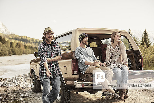 Drei Personen sitzen lächelnd auf dem Rücksitz eines Pickup