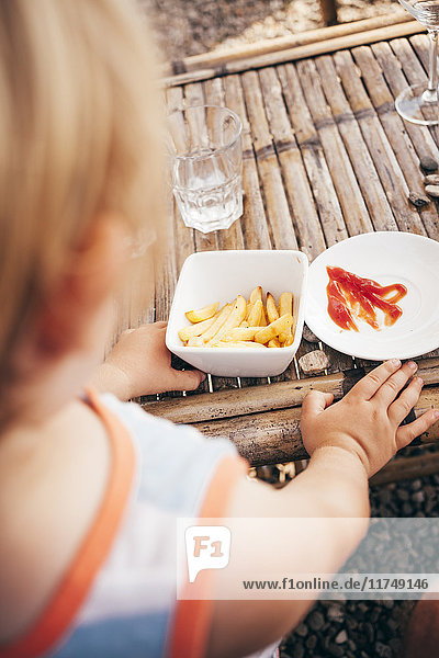 Über-die-Schulter-Ansicht eines Jungen der Pommes Frites und Ketchup isst