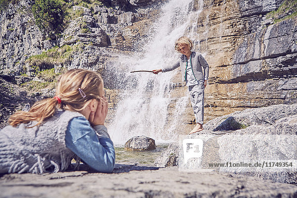 Young girl watching brother  standing beside waterfall