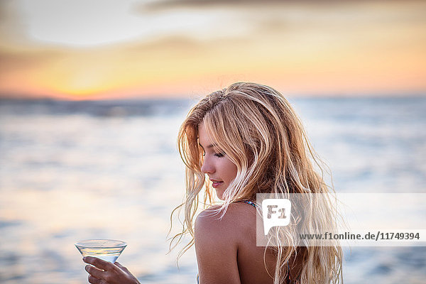 Young woman on beach drinking cocktail at sunset