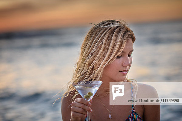 Young woman drinking cocktail on beach at sunset