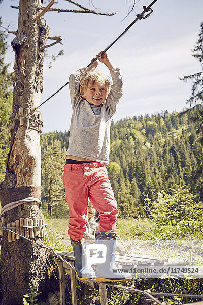 Young boy walking across single rope bridge