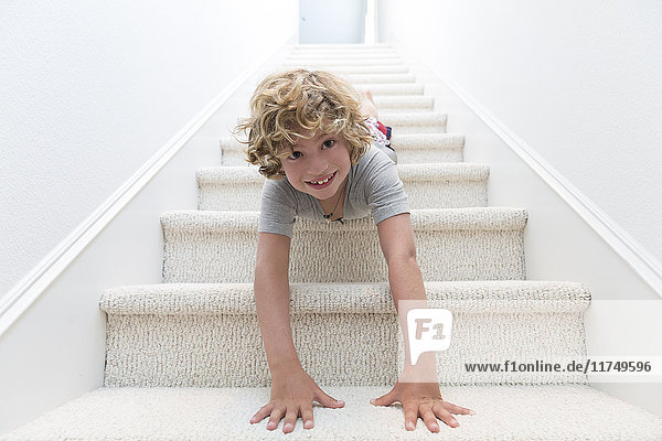 Porträt eines Jungen  der mit dem Kopf voran die Treppe hinunterkriecht