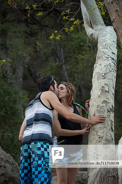 Young couple sharing a kiss whilst holding tree trunk
