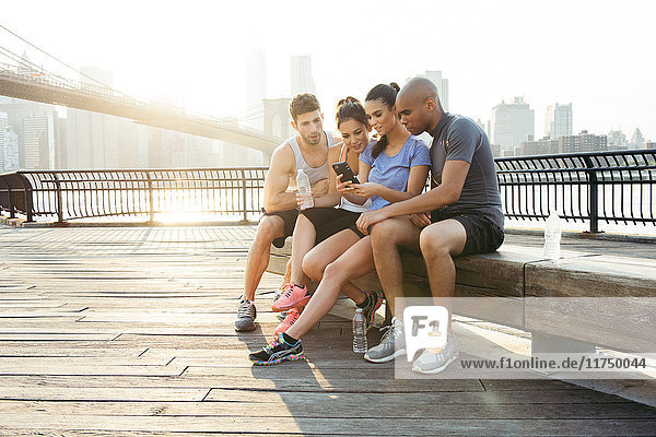 Vier erwachsene  rennende Freunde lesen Smartphone-Text vor der Brooklyn Bridge  New York  USA