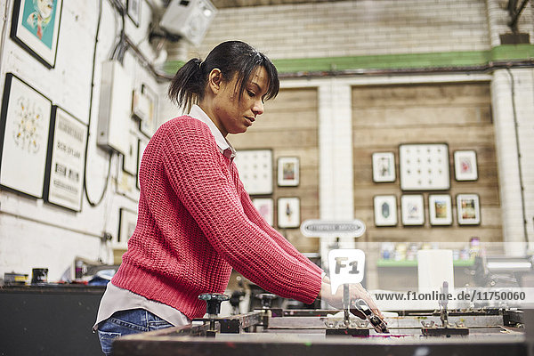 Mittelgroße erwachsene Frau  die die Rakel am Siebdrucker in einer traditionellen Druckwerkstatt benutzt
