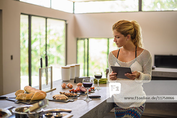 Young woman using digital whilst preparing food in kitchen