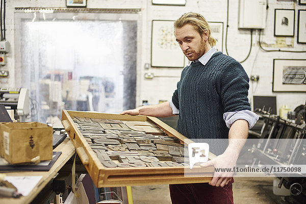 Junger Mann mit Buchdruckschale in traditioneller Druckwerkstatt