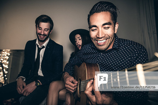 Group of friends sitting on sofa young man playing guitar