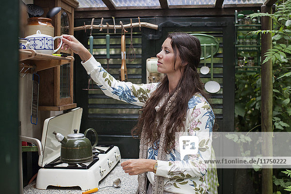 Junge Frau bereitet in offener Hüttenküche Tee zu