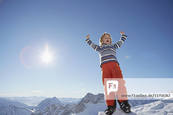 Young boy standing in snowy landscape  celebrating with arms raised  low angle view